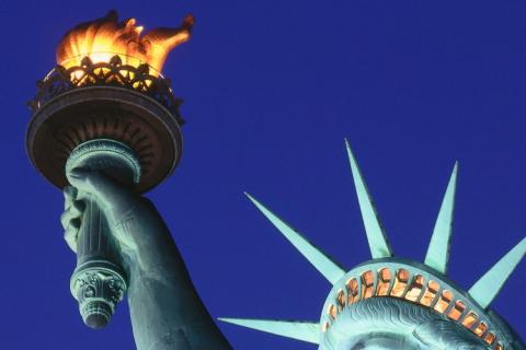 Nahaufnahme der Fackel und eines Teils des Kopfes der Freiheitsstatue gegen einen klaren blauen Himmel.