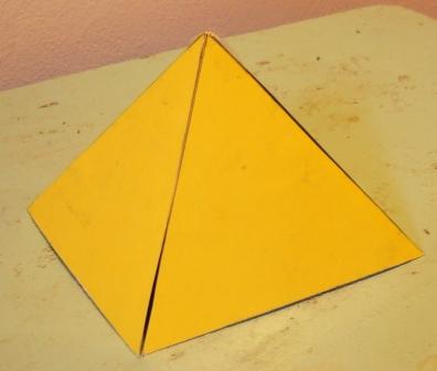 Eine gelbe pyramidenförmige Struktur auf einer abgenutzten Oberfläche, erinnert an einfache geometrische Formen verwendet in der Astronomie zur Darstellung von Strukturen im Universum.