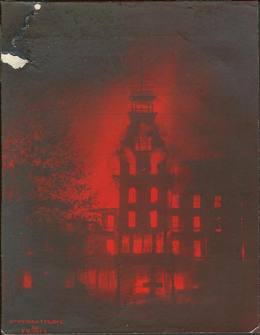 Bild eines historischen Geb&auml;udes bei Nacht, beleuchtet von einem intensiven roten Licht, das eine dramatische und geheimnisvolle Atmosph&auml;re erzeugt. Der Hintergrund erscheint dunkel und verst&auml;rkt den Kontrast mit dem beleuchteten Geb&auml;ude.