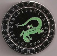 Runde Scheibe mit einem gr&uuml;nen Drachen, umgeben von einem Kreis aus Buchstaben des lateinischen Alphabets, vor einem schwarzen Hintergrund.