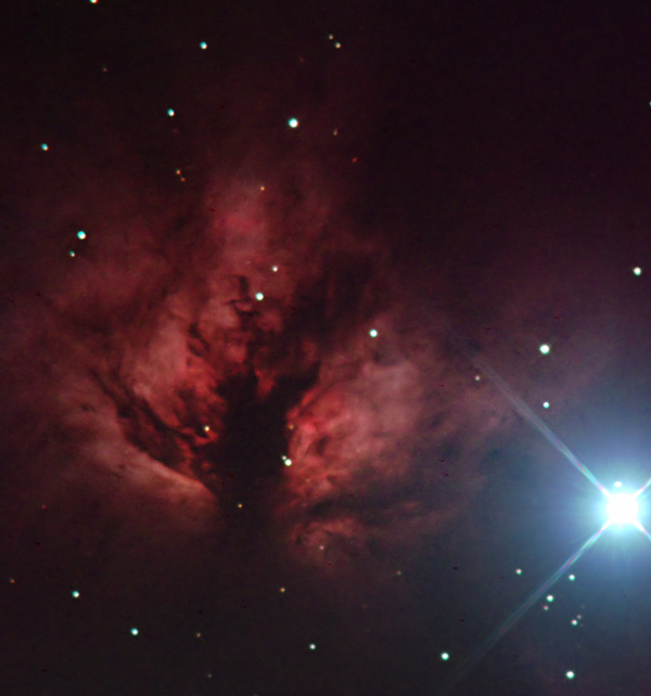 Eine Aufnahme eines kosmischen Nebels, der von zahlreichen Sternen umgeben ist, mit einem besonders hellen Stern strahlt intensiv am rechten Bildrand.