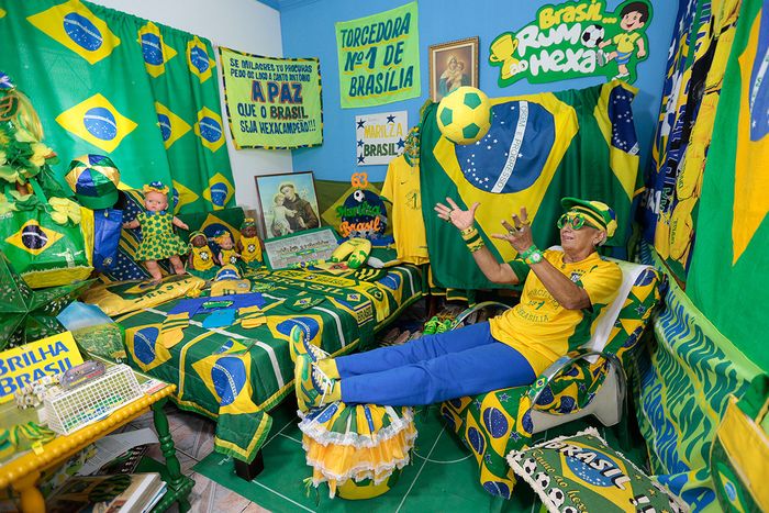 Ein enthusiastischer Fan in einem lebhaft dekorierten Raum, gef&uuml;llt mit zahlreichen Gegenst&auml;nden in Gelb und Gr&uuml;n, die das Fu&szlig;ballteam Brasiliens feiern. Der Raum ist mit Flaggen, Schals und anderen Fanartikeln tapeziert, und der Fan tr&auml;gt eine passende gelb-gr&uuml;ne Kleidung und Accessoires.