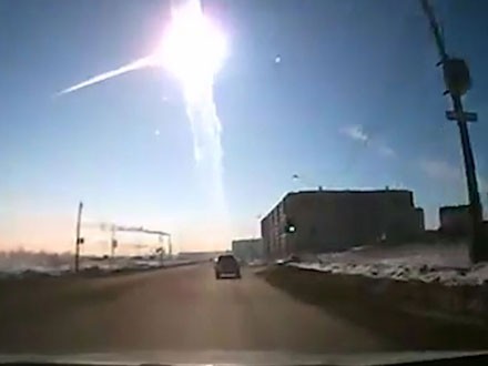 Dashcam-Aufnahme einer winterlichen Stra&szlig;enszene bei Sonnenaufgang mit einem markanten Leuchtstreifen am Himmel, m&ouml;glicherweise ein Meteor, &uuml;ber einer schneebedeckten Landschaft und einer st&auml;dtischen Silhouette.