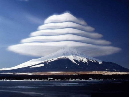 Ein majest&auml;tischer schneebedeckter Berg, &uuml;ber den sich mehrere abgestufte linsenf&ouml;rmige Wolken in einer beeindruckenden Formation t&uuml;rmen, die an eine nat&uuml;rliche Stufenpyramide erinnert. Klare Blaue Himmel im Hintergrund und ein gefrorener See im Vordergrund vervollst&auml;ndigen dieses nat&uuml;rliche Schauspiel.