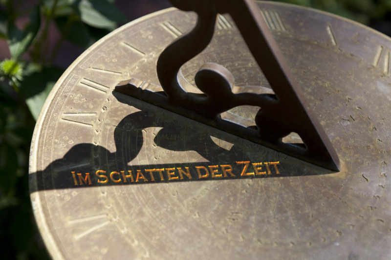 Nahaufnahme einer Sonnenuhr aus Bronze mit eingravierten Symbolen, die die Mazzaroth darstellen k&ouml;nnten, und der Inschrift "Im Schatten der Zeit".