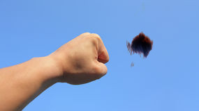 Eine menschliche Hand mit einer Faust, aus der eine Galaxien&auml;hnliche Struktur in Form einer Fussel ausbl&auml;st, vor einem klaren blauen Himmel.