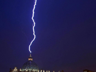 Ein Blitz schl&auml;gt in die Kuppel eines gro&szlig;en, beleuchteten Geb&auml;udes ein, vor einem n&auml;chtlichen Himmel.