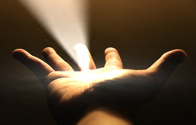 Eine ge&ouml;ffnete Handfl&auml;che, die nach oben gerichtet ist und ein helles, wei&szlig;es Licht einf&auml;ngt, das von oben herabstrahlt, vor einem dunklen Hintergrund.