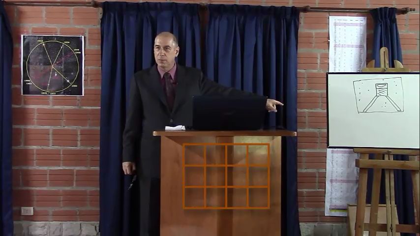 Ein Mann in einem dunklen Anzug steht an einem Rednerpult in einem H&ouml;rsaal. Hinter ihm befinden sich ein Diagramm der Mazzaroth und eine Tafel mit wissenschaftlichen Illustrationen.