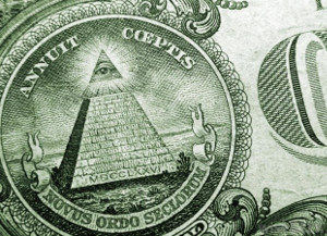 Detailansicht eines Symbols auf einer amerikanischen Ein-Dollar-Note, das eine Pyramide mit einer leuchtenden Spitze und umgebendem lateinischem Text zeigt, daneben eine Darstellung eines Himmelk&ouml;rpers mit Strahleneffekt.